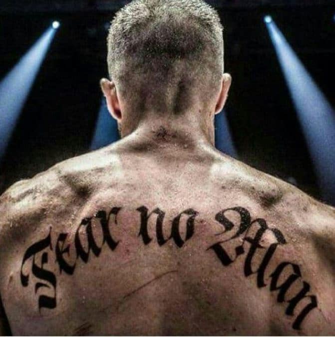 The image is a man's back with a tattoo that reads, "Fear no Man."